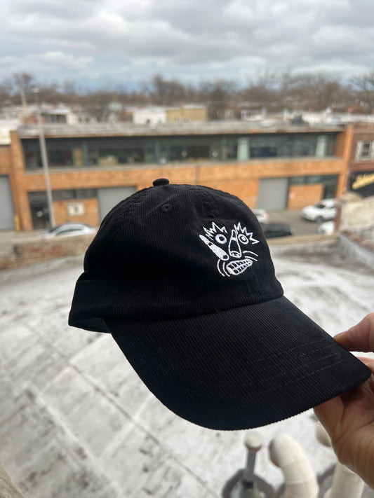 Black cap with a white logo held against an urban background
