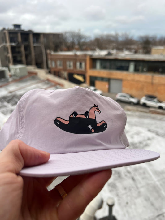 White cap with a black and pink design held in front of a snowy urban landscape.