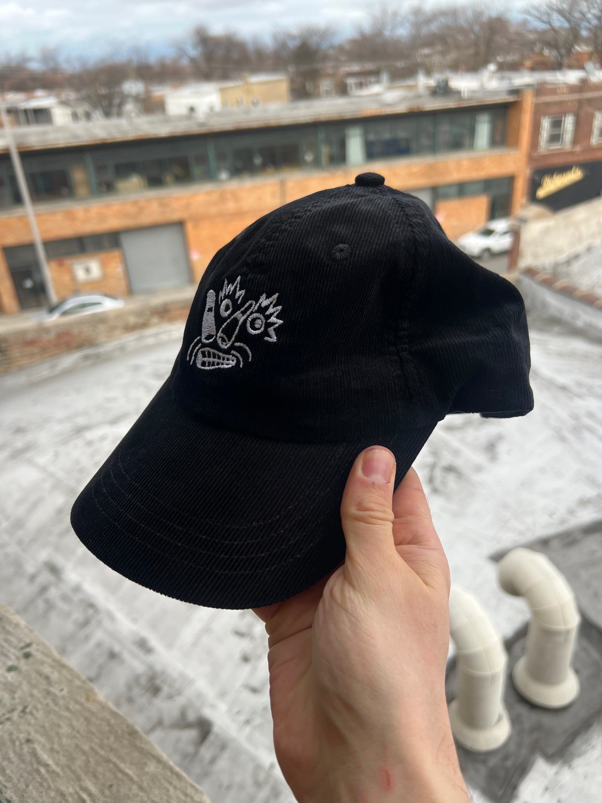 Black cap with white logo held by a hand against an urban background