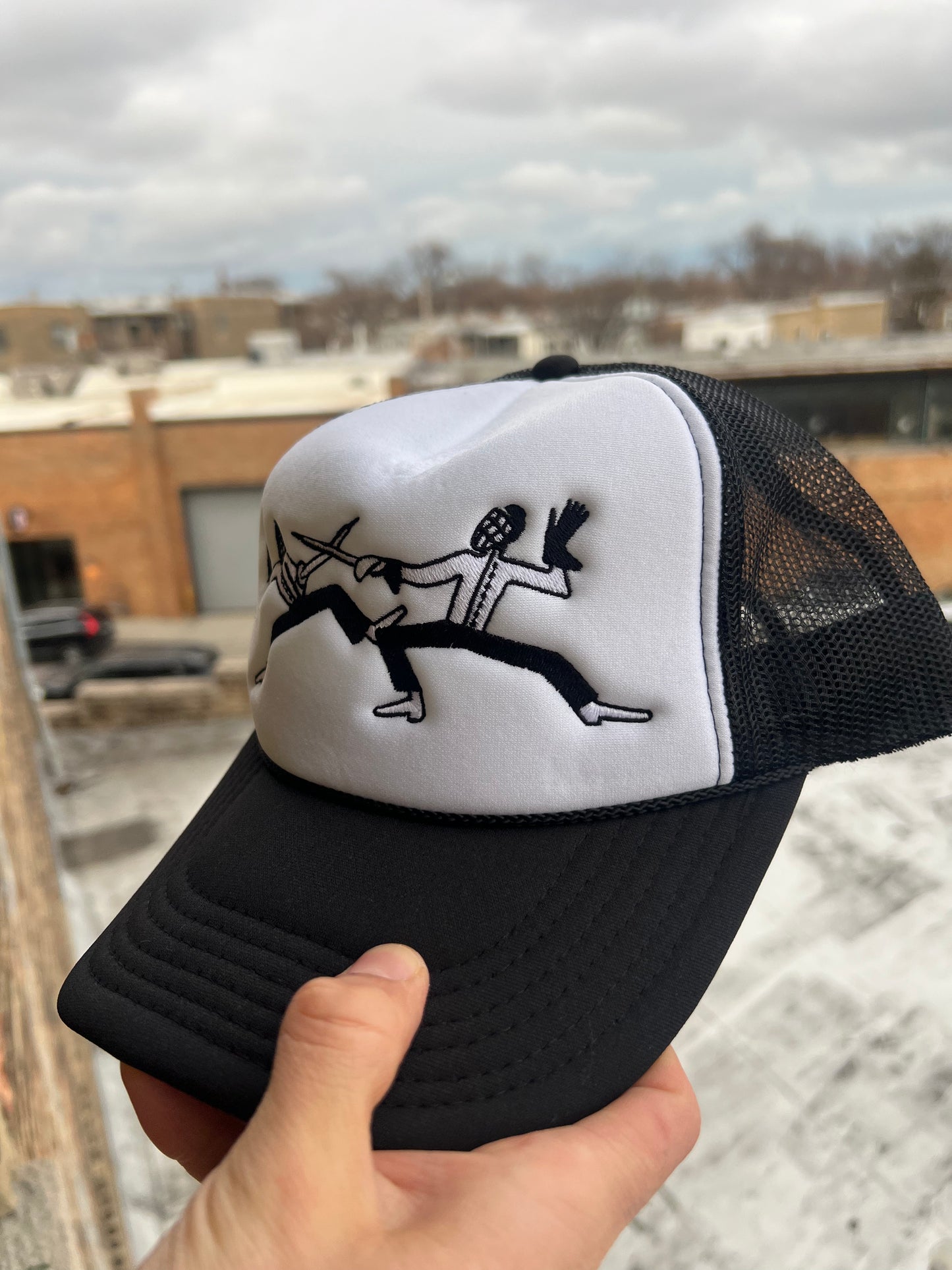 Black and white cap with a design held by a hand against an urban background