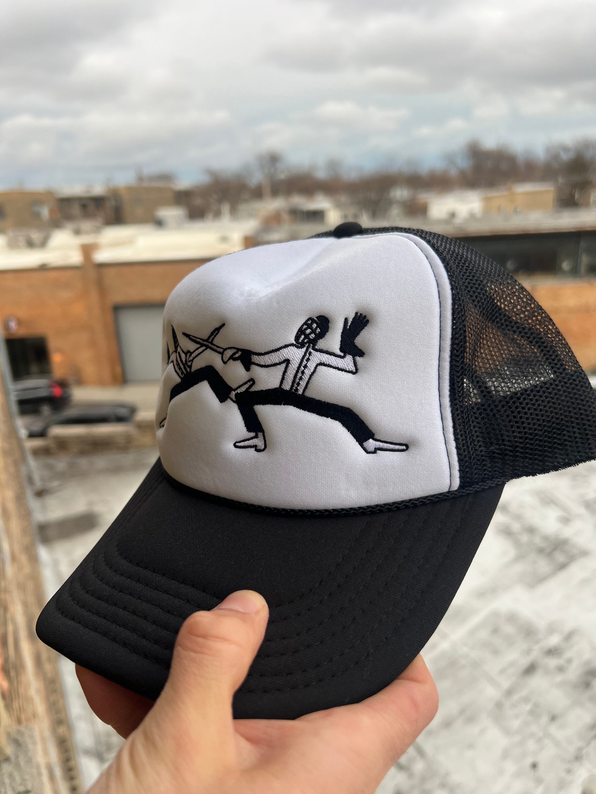 Black and white cap with a design held by a hand against an urban background