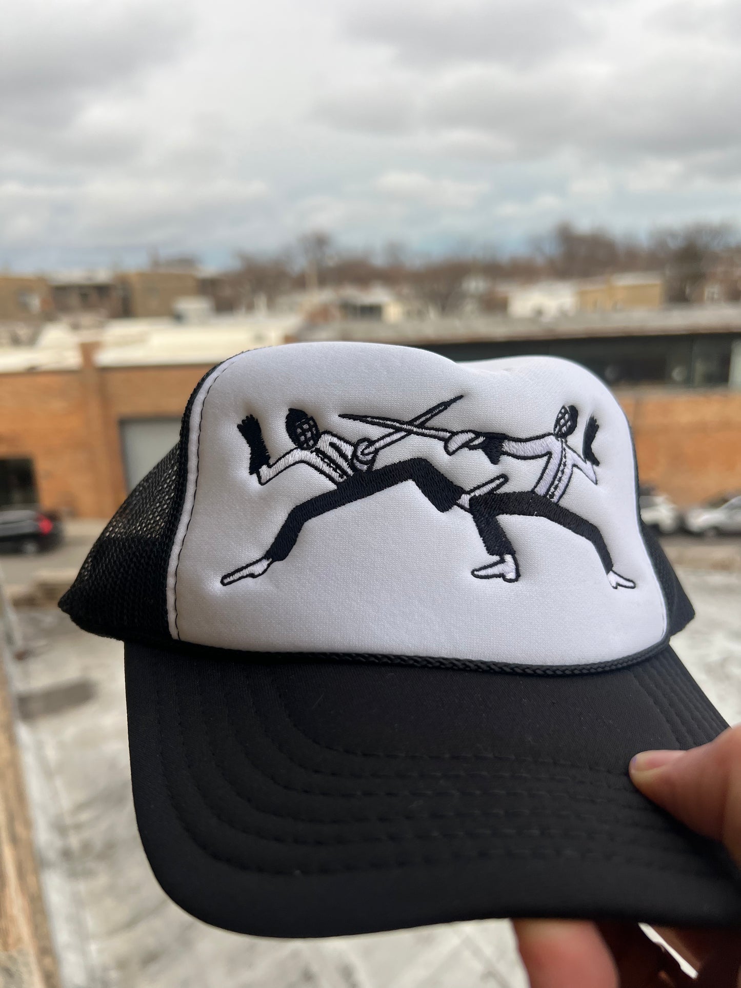Black and white cap with graphic design held against an urban background