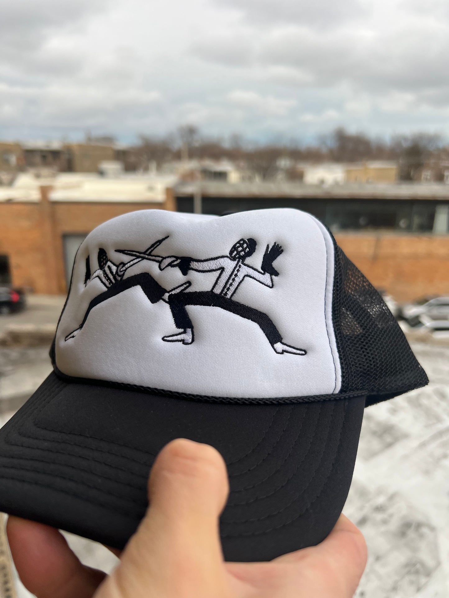 Black and white cap with graphic design held in front of a snowy landscape.