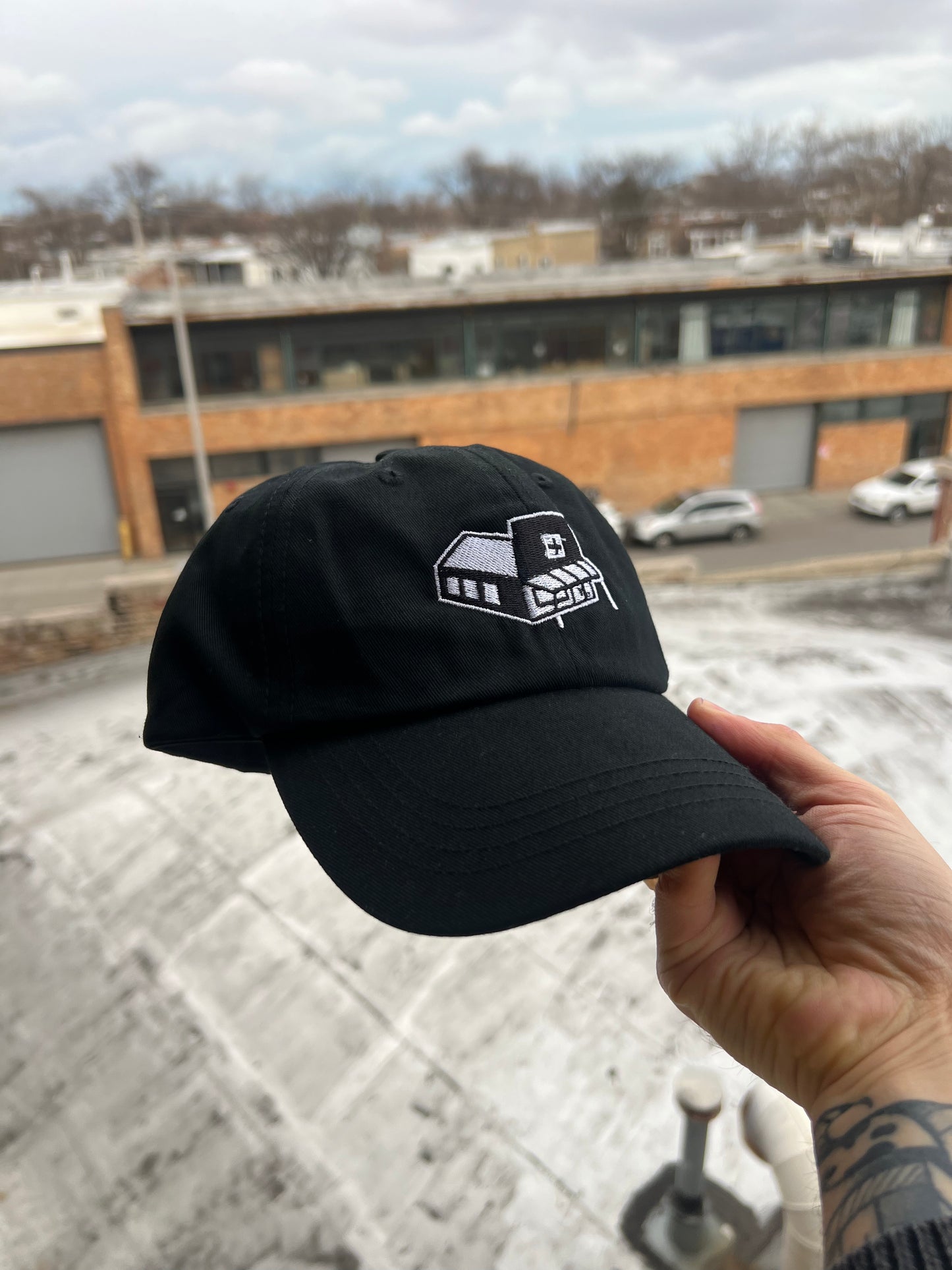 Black cap with a white logo held by a hand against an urban background