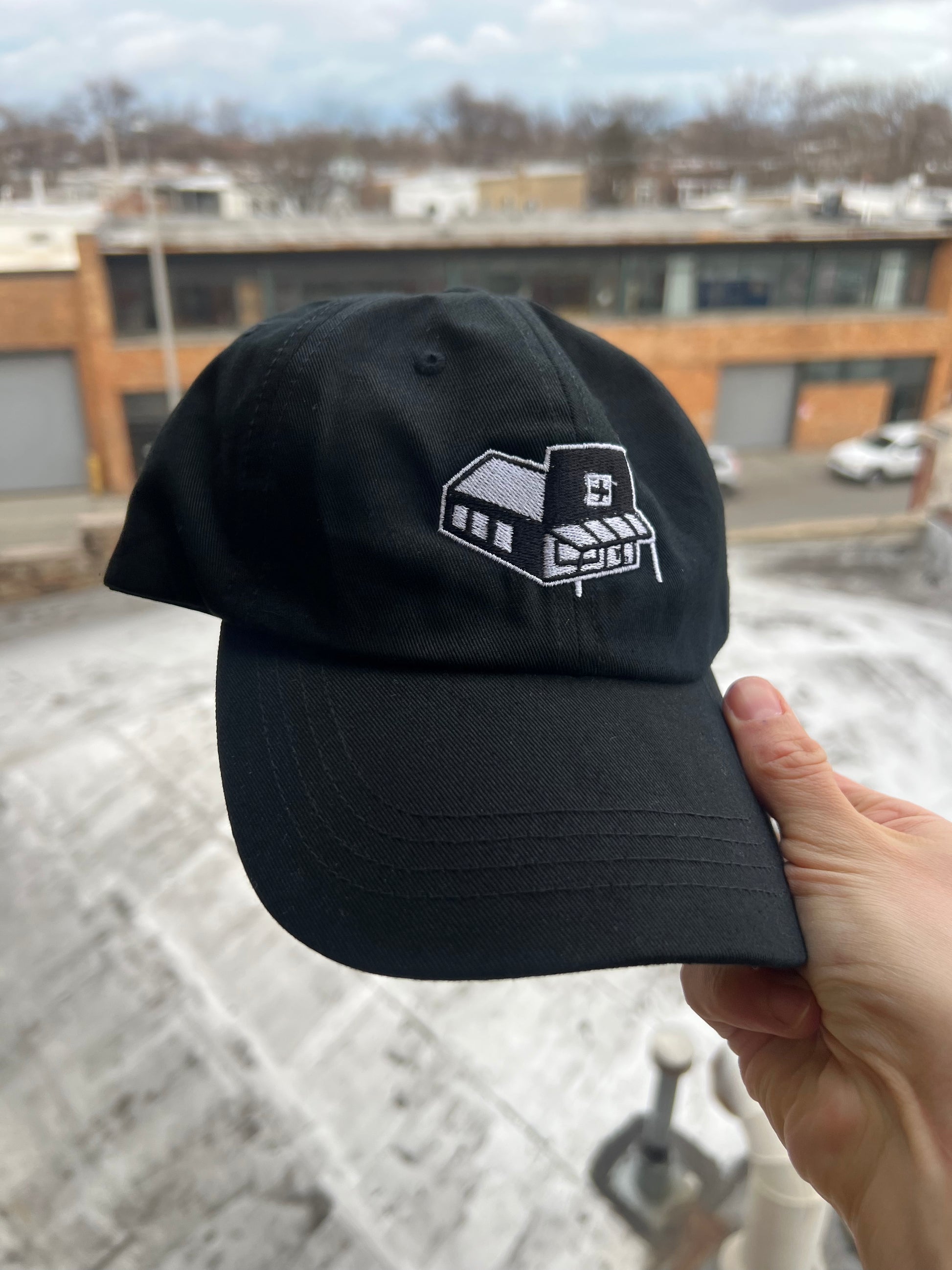 Black cap with a white logo held by a hand against an urban background