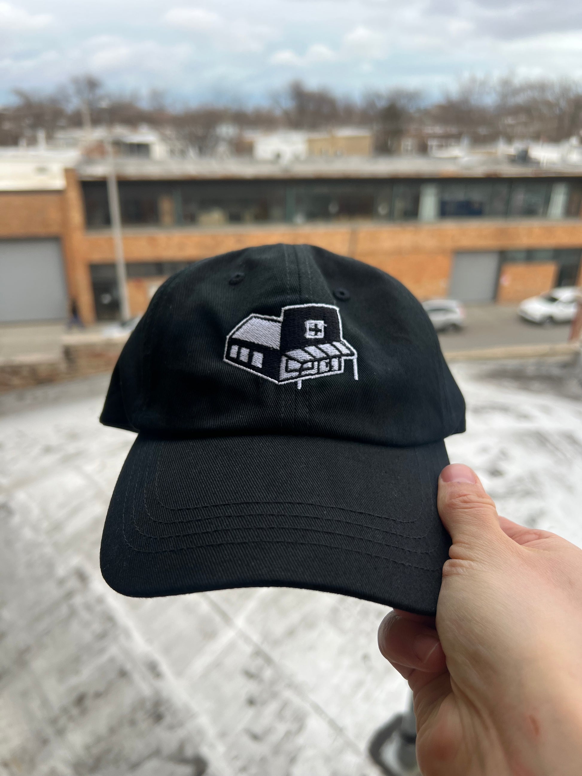 Black cap with a logo held by a hand against an outdoor background