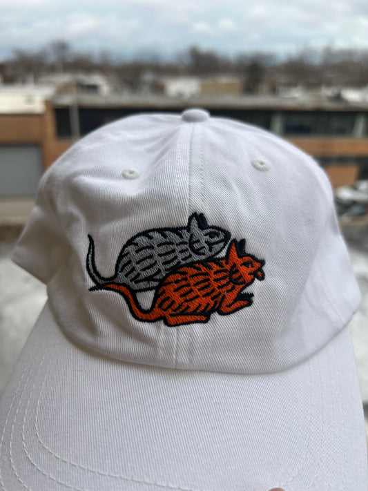 White cap with embroidered design of a rat and lion on a blurred background