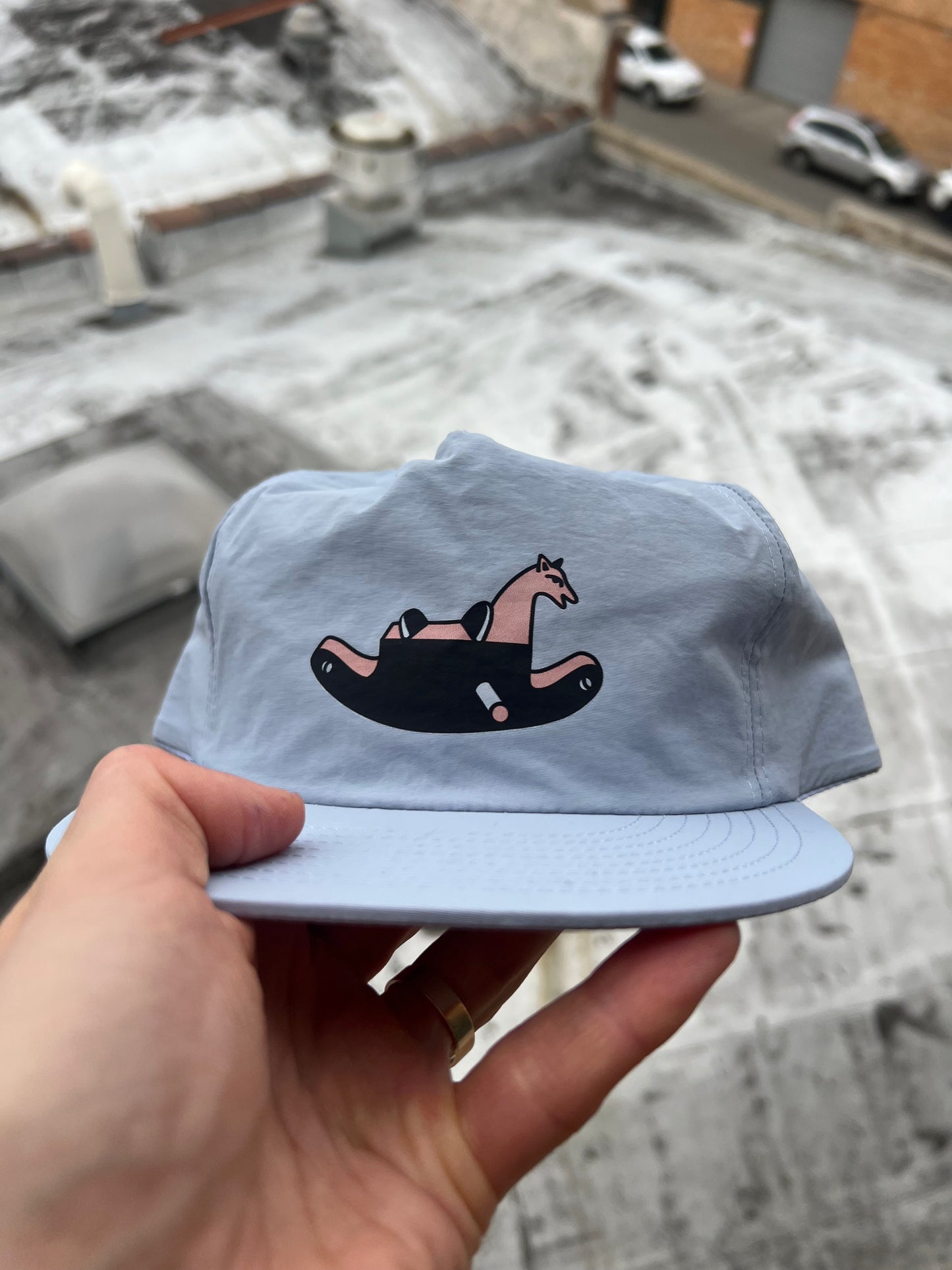 Light blue cap with a graphic design held by a hand, snowy ground in the background