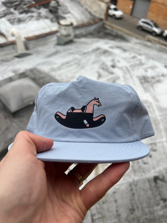 Light blue cap with a graphic design held by a hand, snowy ground in the background