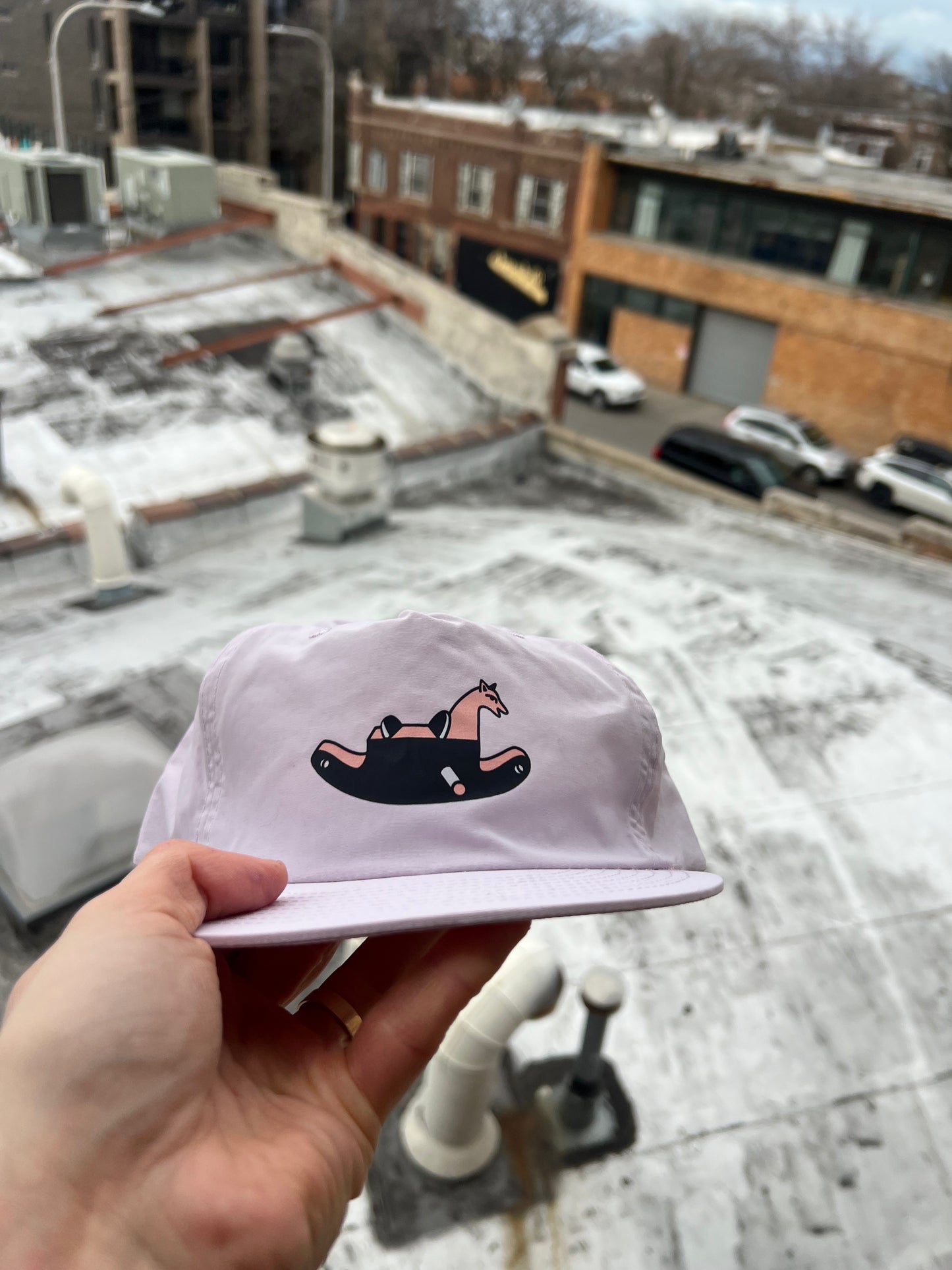 Pink cap with a horse design held up against a snowy rooftop background